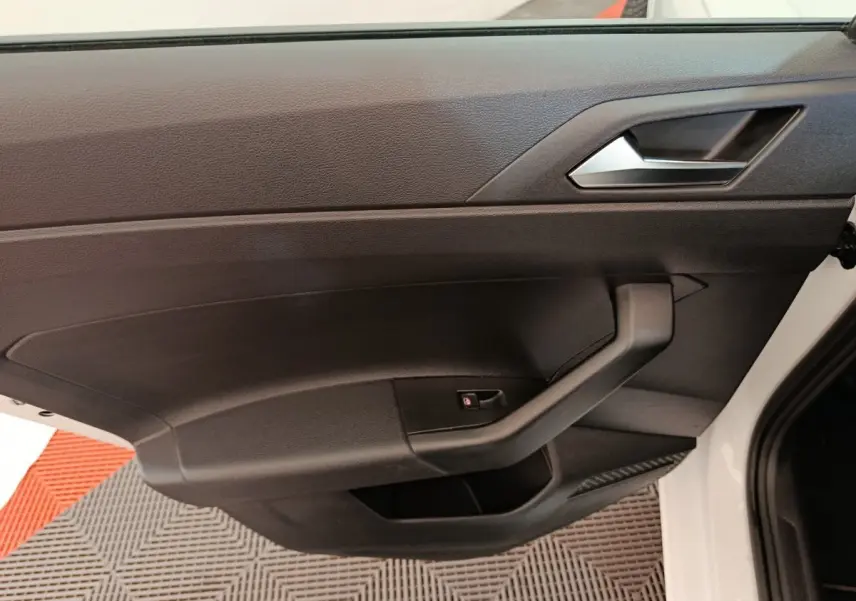 Gros plan sur la porte intérieure côté gauche noire d'une Volkswagen Polo blanche 2020, avec poignée et bouton de verrouillage.