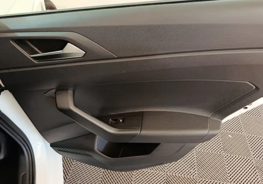 Vue rapprochée de la porte avant gauche noire d'une Volkswagen Polo blanche avec poignée intégrée et bouton de verrouillage.