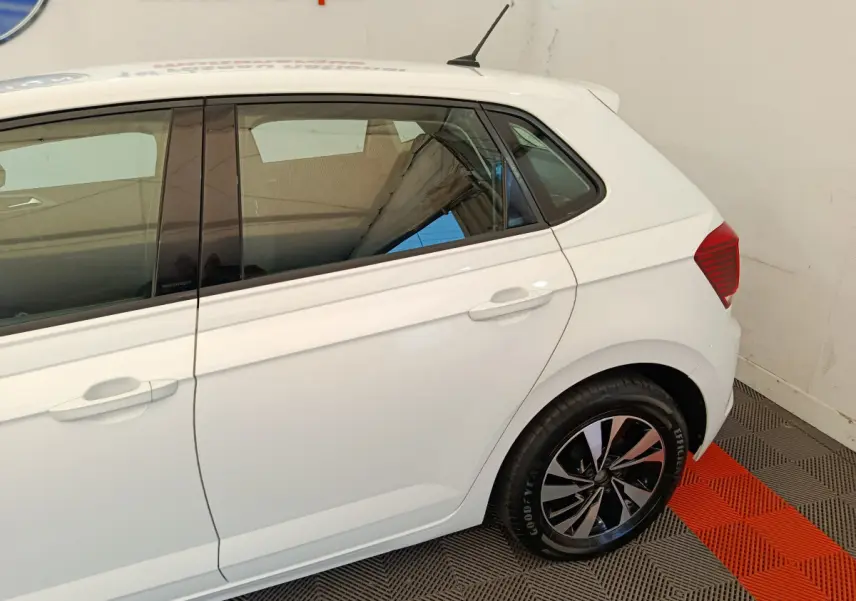 Vue latérale droite d'une Volkswagen Polo blanche 2020 avec jantes alliage et vitres teintées en intérieur showroom.