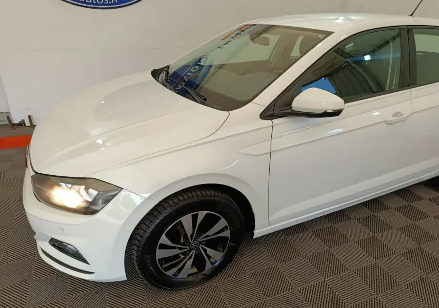 Vue 3/4 avant droit d'une Volkswagen Polo blanche avec phares allumés et jantes alliage noires.