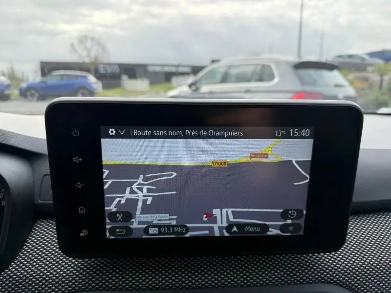 Vue intérieure centrée sur l'écran tactile du GPS du Dacia Jogger gris 2025, avec tableau de bord et extérieur flou en arrière-plan.
