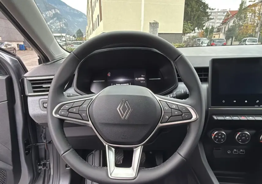 Vue intérieure centrée sur le volant cuir multifonctions de la Renault Clio gris rafale avec tableau de bord et écran tactile.
