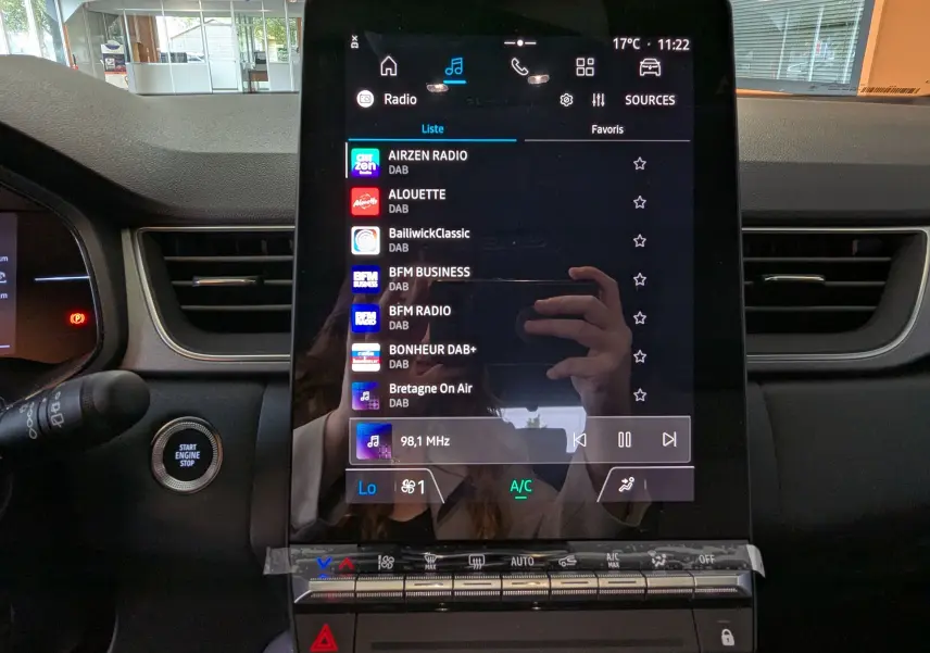 Écran tactile central allumé du Renault Captur E-Tech 2025, affichant les stations radio DAB, avec commandes climatisation en dessous.