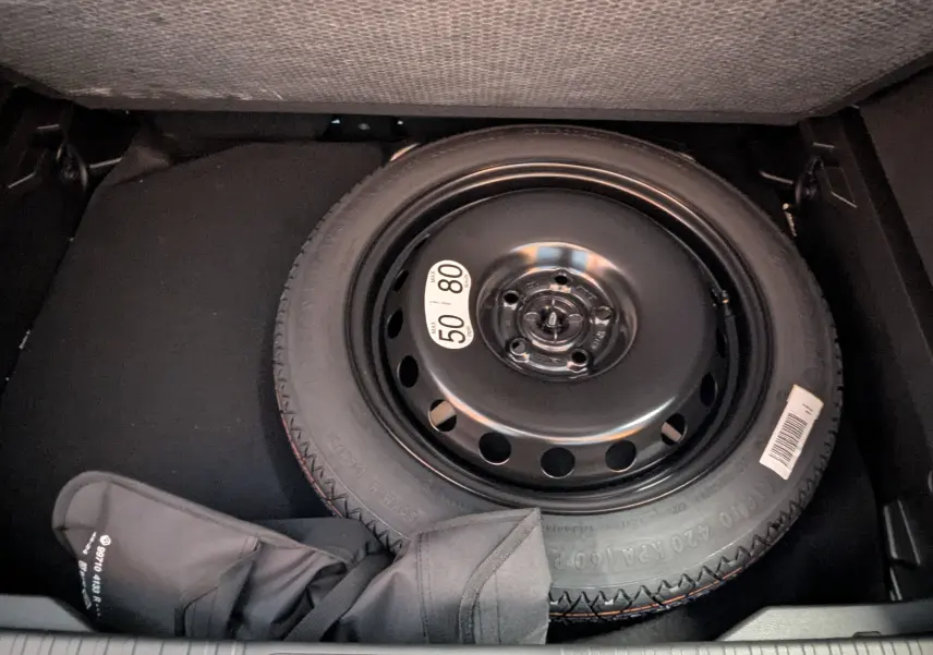 Roue de secours compacte noire dans le coffre d'un Renault Captur E-Tech hybride 2025, avec housse de protection partielle.