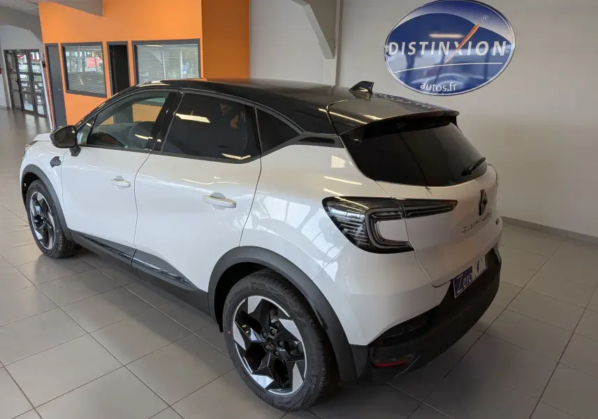 Vue 3/4 arrière droite du Renault Captur E-Tech blanc nacré avec toit noir et jantes noires en showroom.