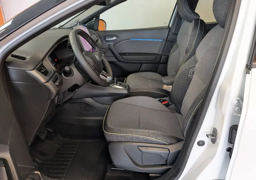 Intérieur côté conducteur du Renault Captur blanc nacré 2025, sièges tissu gris avec surpiqûres jaunes et tableau de bord moderne.