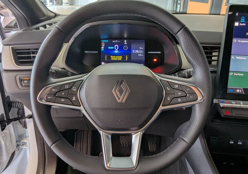 Vue rapprochée du volant en cuir noir perforé du Renault Captur E-Tech 2025, avec tableau de bord numérique allumé.