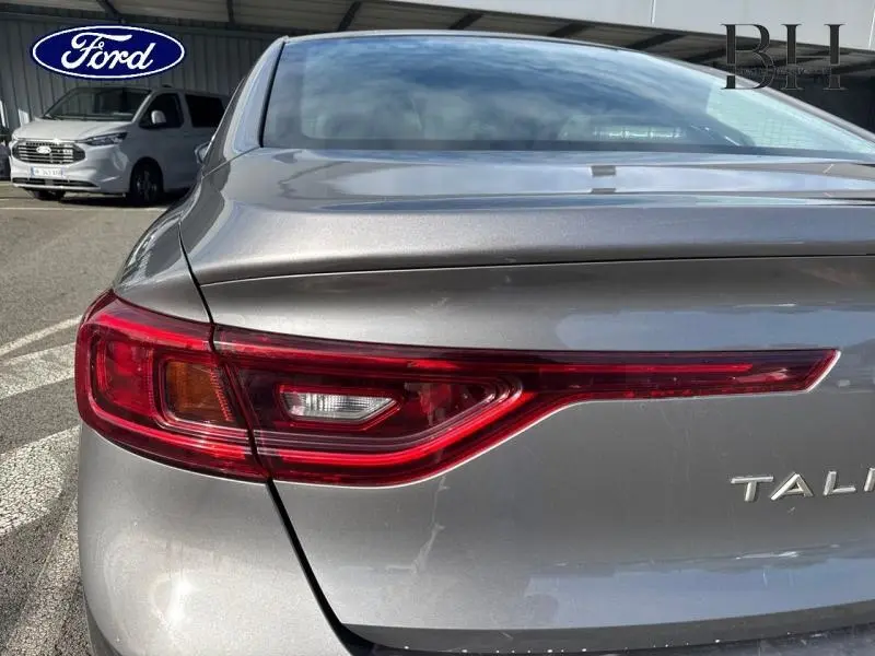 Gros plan sur le feu arrière gauche d'une Renault Talisman gris Cassiopée, avec le logo et le nom partiel visibles.