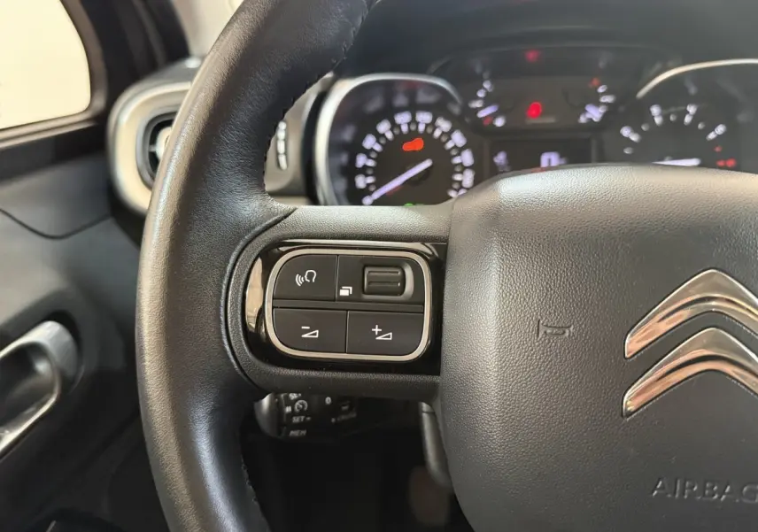 Gros plan sur le volant cuir noir de la Citroën C3 2019 avec commandes audio et tableau de bord en arrière-plan flou.