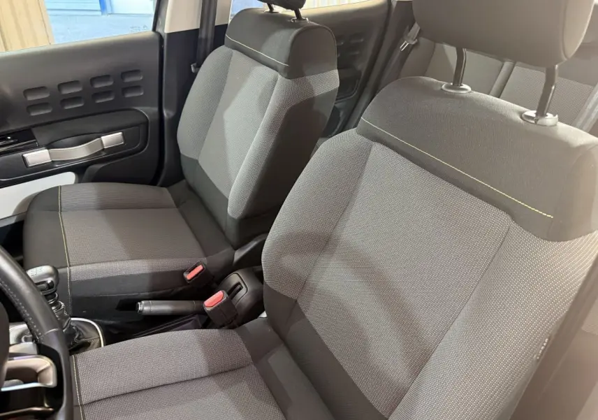 Vue intérieure rapprochée sur les sièges avant gris foncé de la Citroën C3 avec coutures jaunes et poignée de frein à main.
