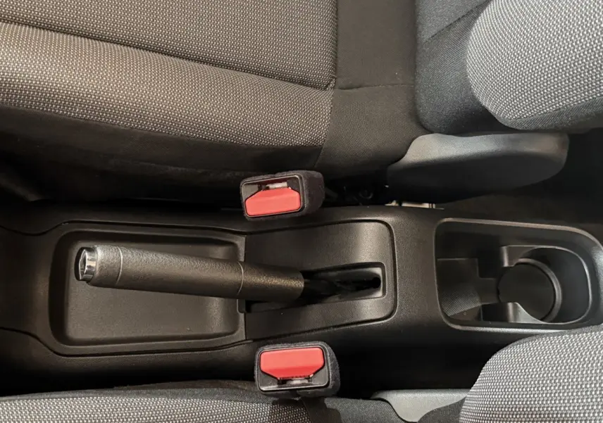 Vue plongeante sur la console centrale noire avec frein à main et ceintures rouges entre sièges gris foncé du Citroën C3.