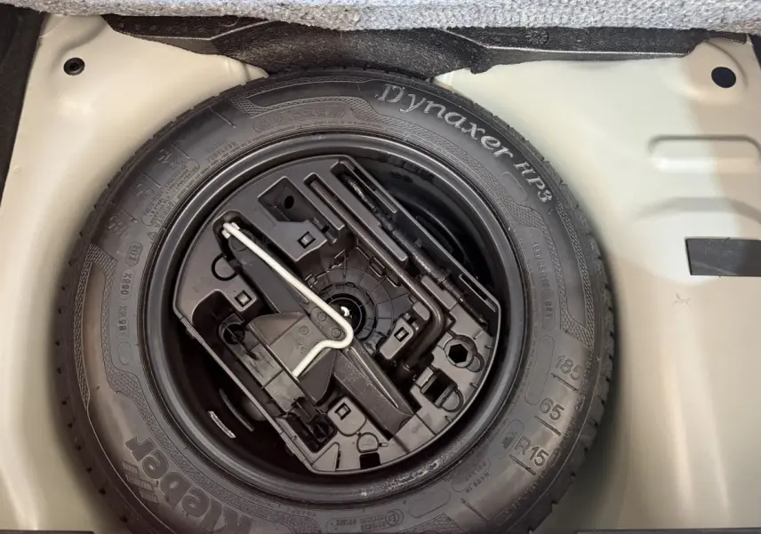 Gros plan sur la roue de secours noire et ses outils dans le coffre gris clair d'une Citroën C3 2019 Shine Business.