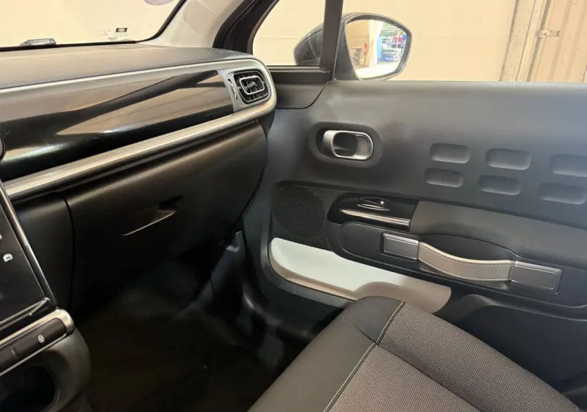 Intérieur côté passager de la Citroën C3 gris clair, montrant la porte avec poignée beige et tableau de bord noir.