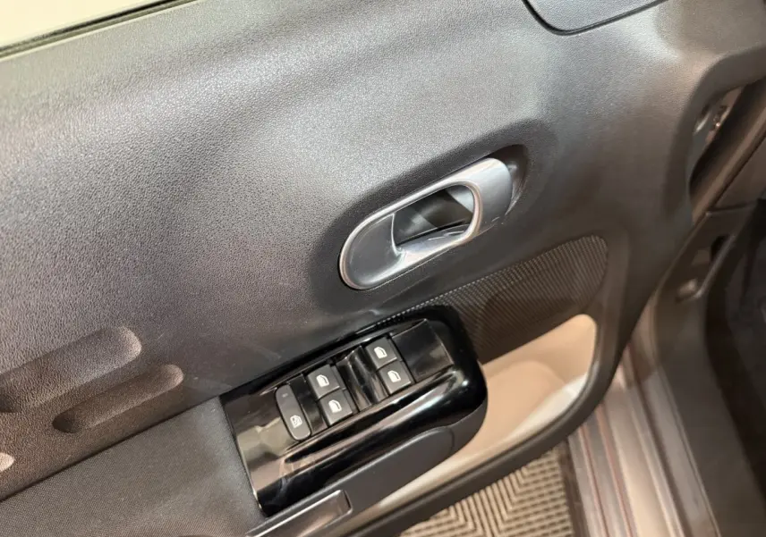 Gros plan sur la commande des vitres et la poignée intérieure côté gauche d'une Citroën C3 gris clair 2019.