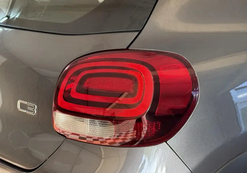 Gros plan sur le feu arrière droit rouge et blanc d'une Citroën C3 gris clair, avec logo C3 visible sur la carrosserie.