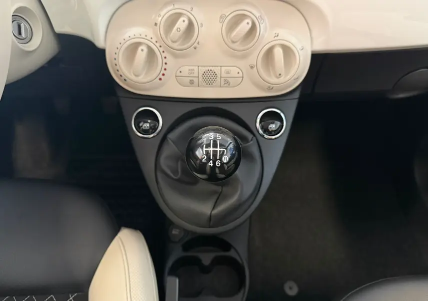 Vue rapprochée du levier de vitesses manuel noir et des commandes de climatisation crème dans une Fiat 500 blanche Dolcevita 2022.