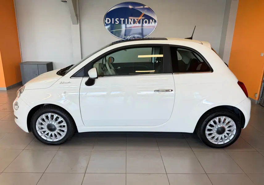 Profil côté gauche de la Fiat 500 Dolcevita blanche Bossa Nova, avec jantes spécifiques et toit ouvrant visible en intérieur showroom.