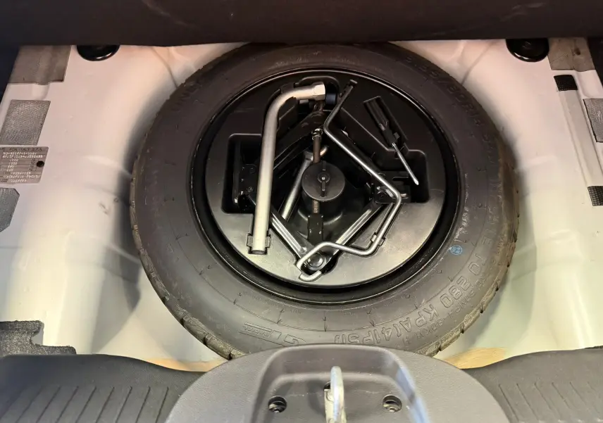 Vue plongeante sur la roue de secours et les outils de bord dans le coffre blanc d'une Fiat 500 2022 Bossa Nova White.