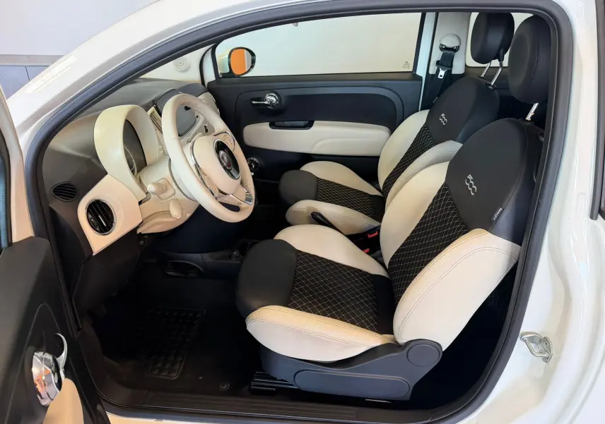 Vue intérieure côté conducteur du Fiat 500 2022 blanc Bossa Nova, sièges bicolores noirs et blancs avec logo 500 brodé.