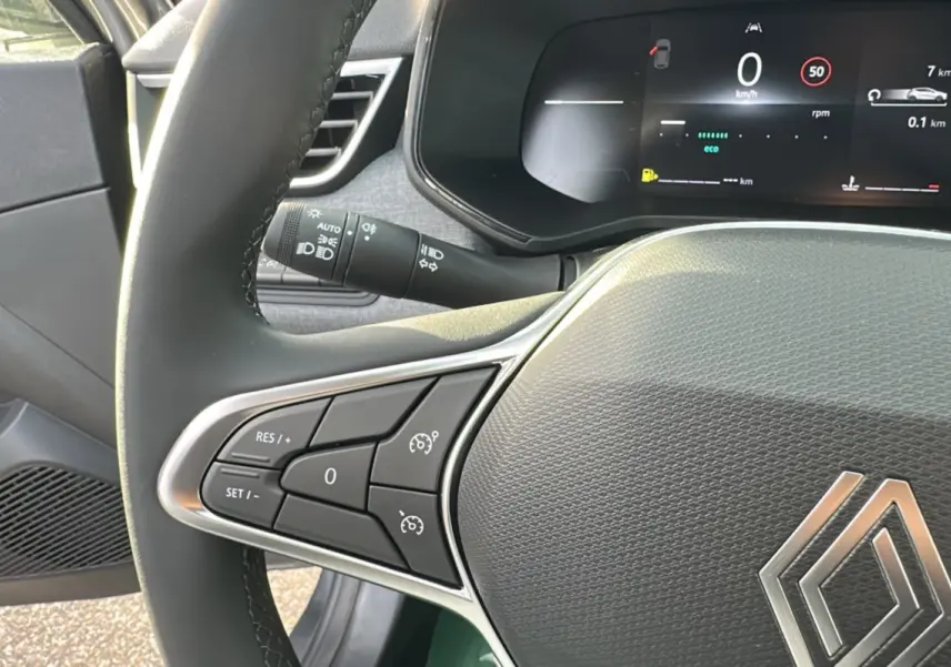 Gros plan sur le volant multifonctions de la Renault Clio gris schiste, avec commandes de régulateur et tableau de bord numérique.