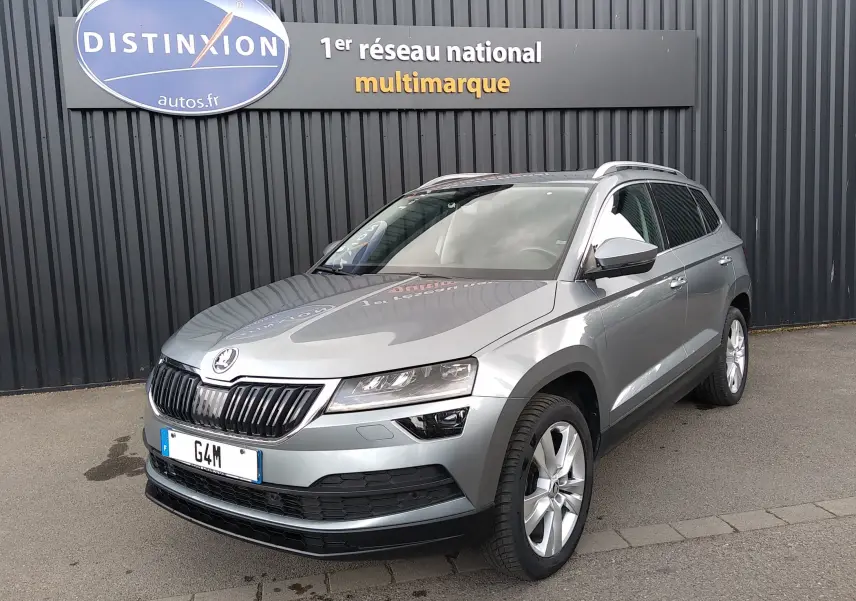 SUV Skoda Karoq gris en 3/4 avant droit, avec calandre noire et jantes alliage, stationné devant un mur noir.