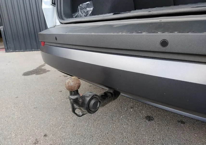 Vue rapprochée de l'attelage arrière rouillé d'un Skoda Karoq gris, coffre ouvert sur un sol goudronné.
