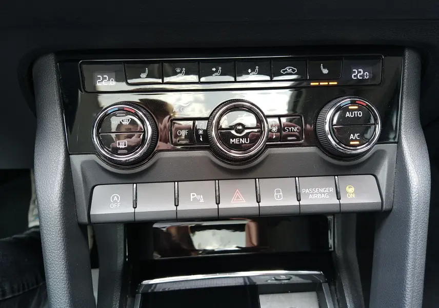 Vue rapprochée de la console centrale du Skoda Karoq gris 2022, montrant les commandes de climatisation et les boutons de sécurité.