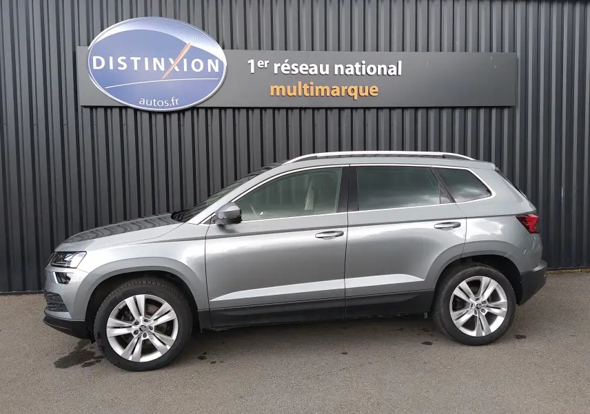 Vue latérale droite d'un Skoda Karoq gris 2022 avec jantes alliage et barres de toit chromées.