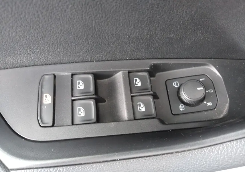 Gros plan sur les commandes de lève-vitres et réglage des rétroviseurs côté conducteur d'un Skoda Karoq gris 2022.