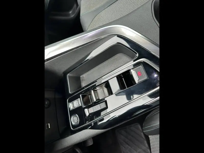 Gros plan sur la console centrale noire brillante du Peugeot 3008 Hybride Rechargeable, avec commandes de boîte auto et frein électrique.