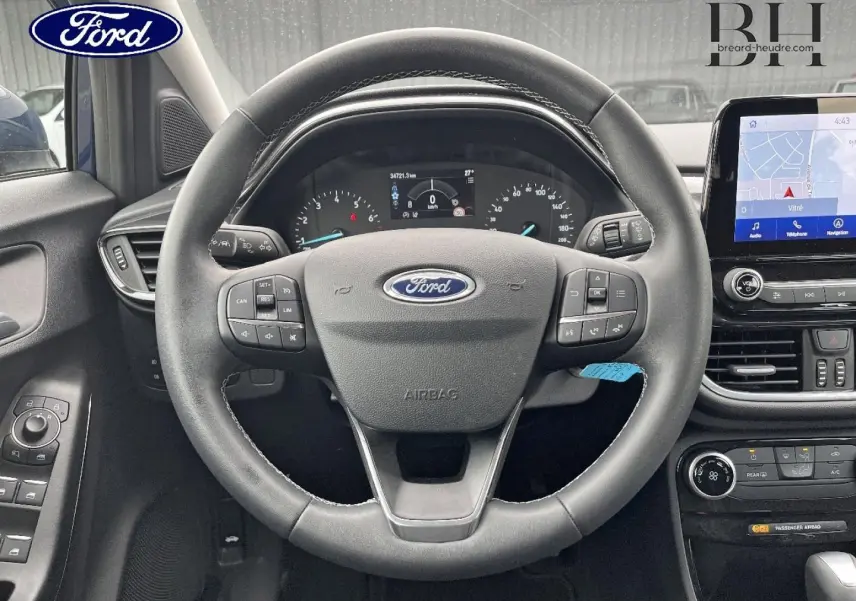 Vue intérieure centrée sur le volant multifonction du Ford Puma bleu avec tableau de bord et écran tactile visible.