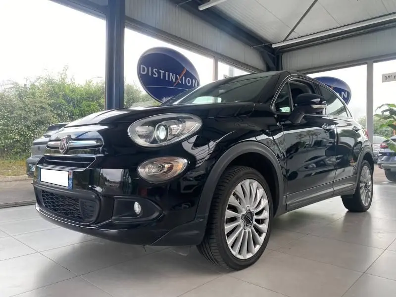 Vue 3/4 avant droit d'une FIAT 500X noire brillante avec jantes alliage et phares xénon en showroom.