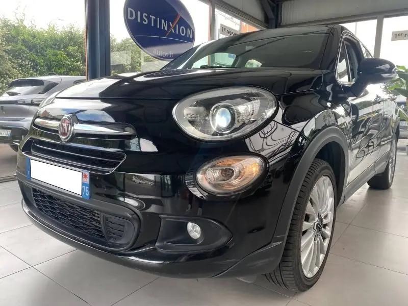 Vue 3/4 avant droite d'une FIAT 500X noire avec phares allumés et jantes alliage en showroom.