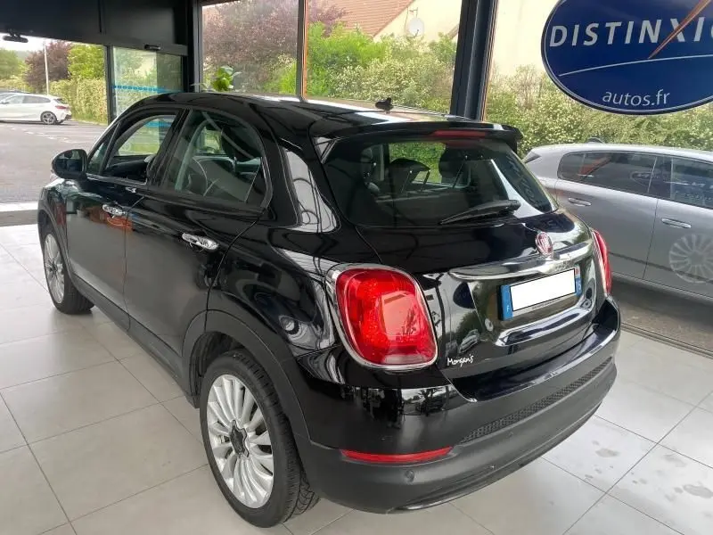 Vue 3/4 arrière droite d'une FIAT 500X noire avec jantes alliage et feux arrière rouges dans un showroom.