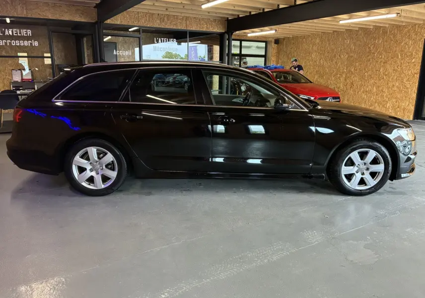 Audi A6 Avant noire vue de profil côté gauche dans un garage avec jantes argentées et vitres teintées.