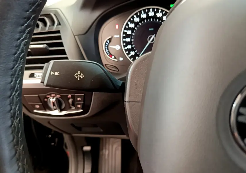 Gros plan sur la manette de commande à gauche du volant du BMW X3 noir, avec tableau de bord et compteurs visibles.