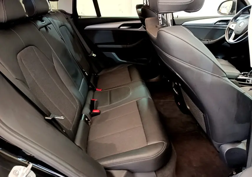 Vue intérieure arrière du BMW X3 noir 2020, sièges en cuir et tissu avec surpiqûres blanches visibles.