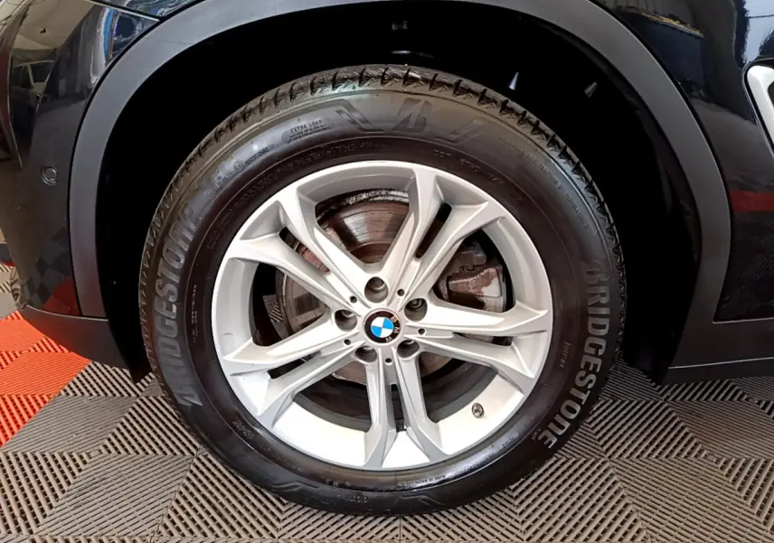 Gros plan sur la roue avant gauche noire d'un BMW X3 xDrive20d 2020 avec jante alliage et pneu Bridgestone.