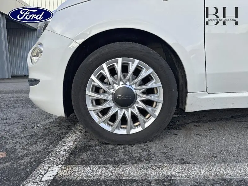 Gros plan sur la roue avant gauche d'une Fiat 500 blanche Bossa Nova avec jante alu au design étoilé.