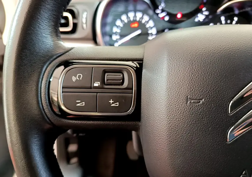 Gros plan sur le volant cuir noir de la Citroën C3 2019 avec commandes audio et tableau de bord lumineux en arrière-plan.