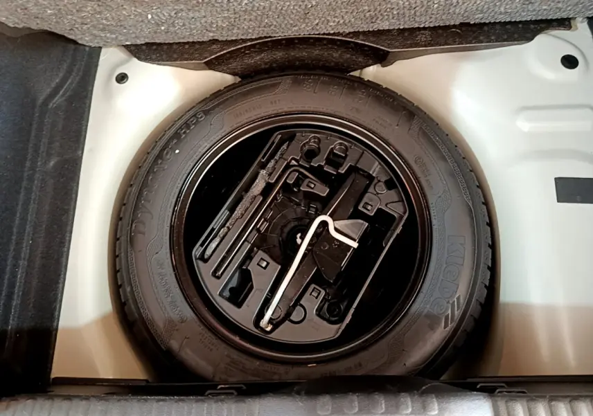 Roue de secours noire avec outils intégrés dans le coffre blanc d'une Citroën C3 blanche, vue de dessus.