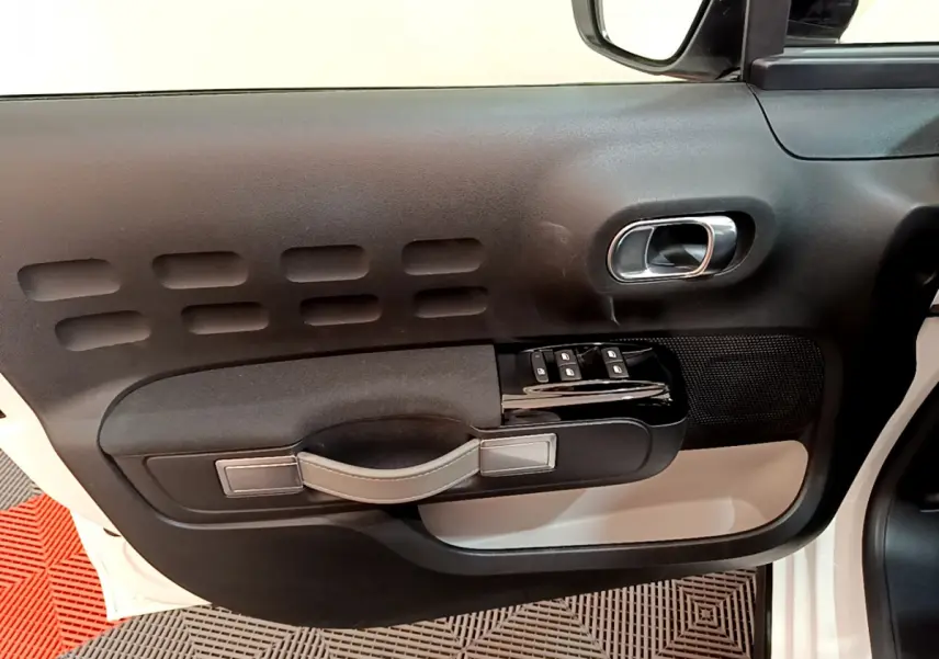 Vue rapprochée de la porte côté gauche d'une Citroën C3 blanche, avec poignée noire et commandes de vitres.