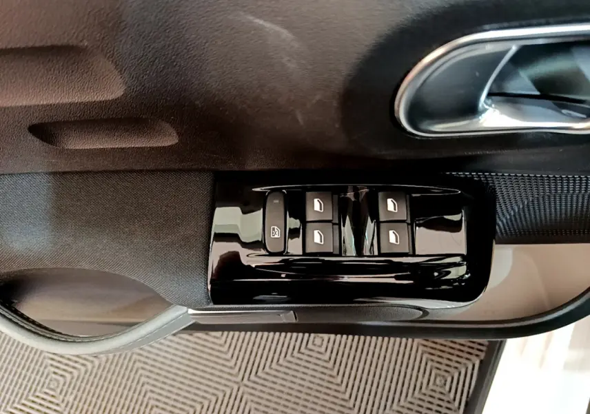 Commandes des vitres électriques sur la porte côté conducteur d'une Citroën C3 blanche, vue rapprochée intérieure.