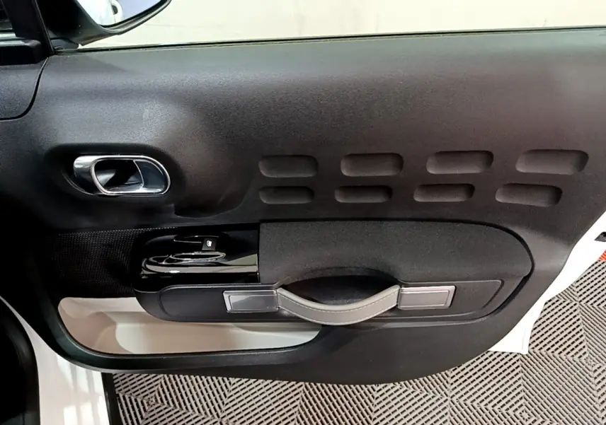 Vue côté gauche de la porte intérieure noire et beige d'une Citroën C3 blanche avec poignée et commandes de vitres.