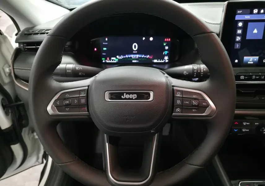 Vue rapprochée du volant Jeep Compass 2024 noir avec commandes intégrées et tableau de bord numérique allumé