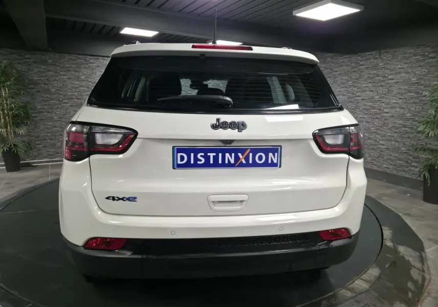 Vue arrière d'un Jeep Compass blanc hybride rechargeable avec logo 4xe et plaque Distinxion dans un showroom.