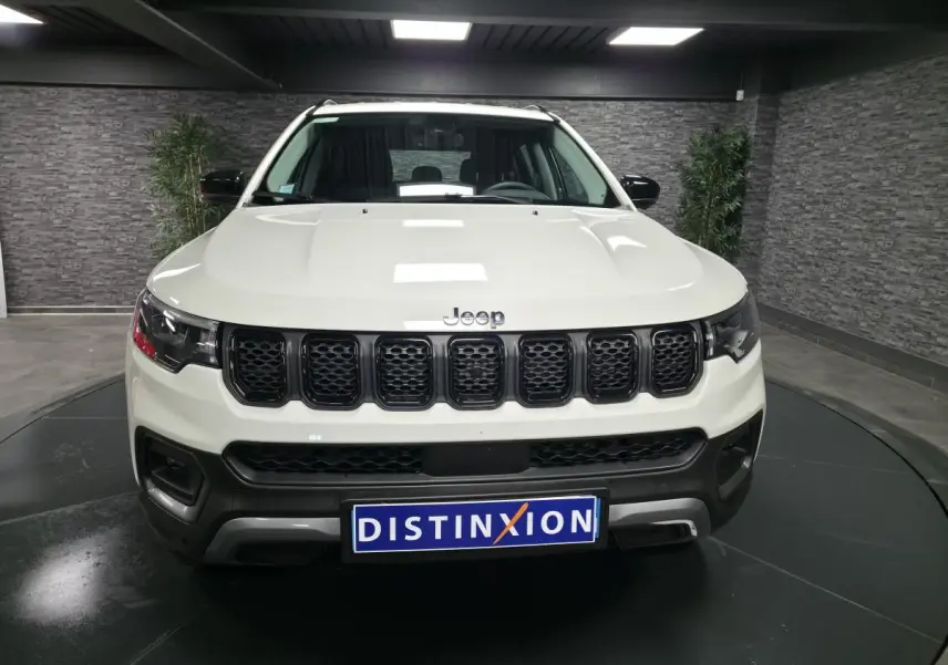 Vue frontale d'un Jeep Compass blanc avec calandre noire et plaque Distinxion en intérieur showroom.