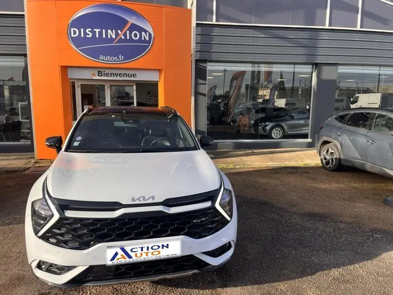 Vue avant d'un Kia Sportage blanc nacré avec calandre noire et toit panoramique, stationné devant un concessionnaire.