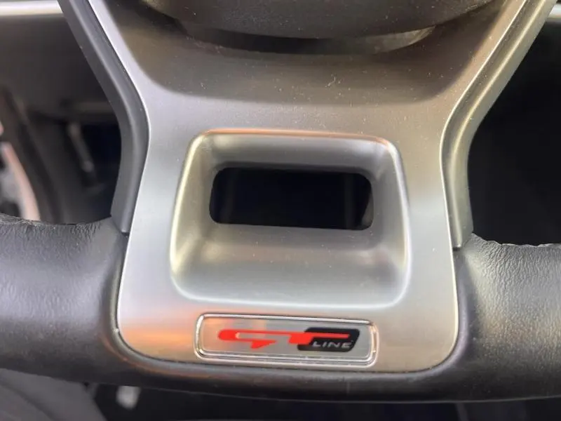 Gros plan sur le volant cuir noir avec insert métal et logo rouge GT-Line du Kia Sportage blanc Sensation nacré 2022.
