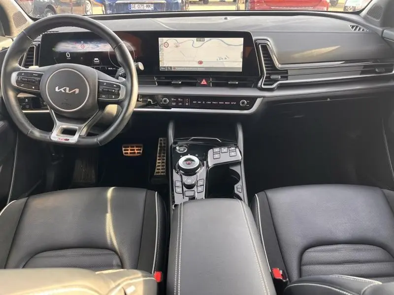 Vue intérieure avant du Kia Sportage 2022 avec tableau de bord noir, volant cuir multifonction et écran tactile panoramique.